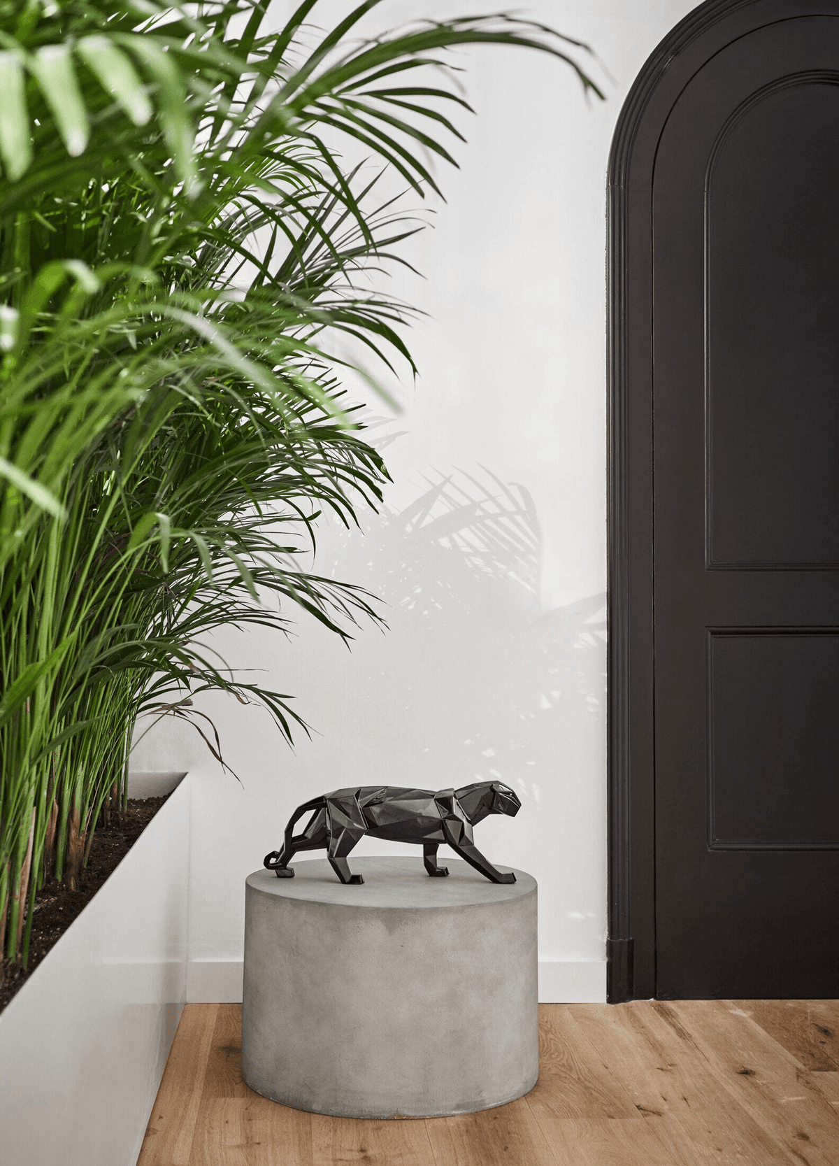 Lladró - Panther Sculpture - Glazed Black displayed on a concrete pedestal surrounded by green plants.