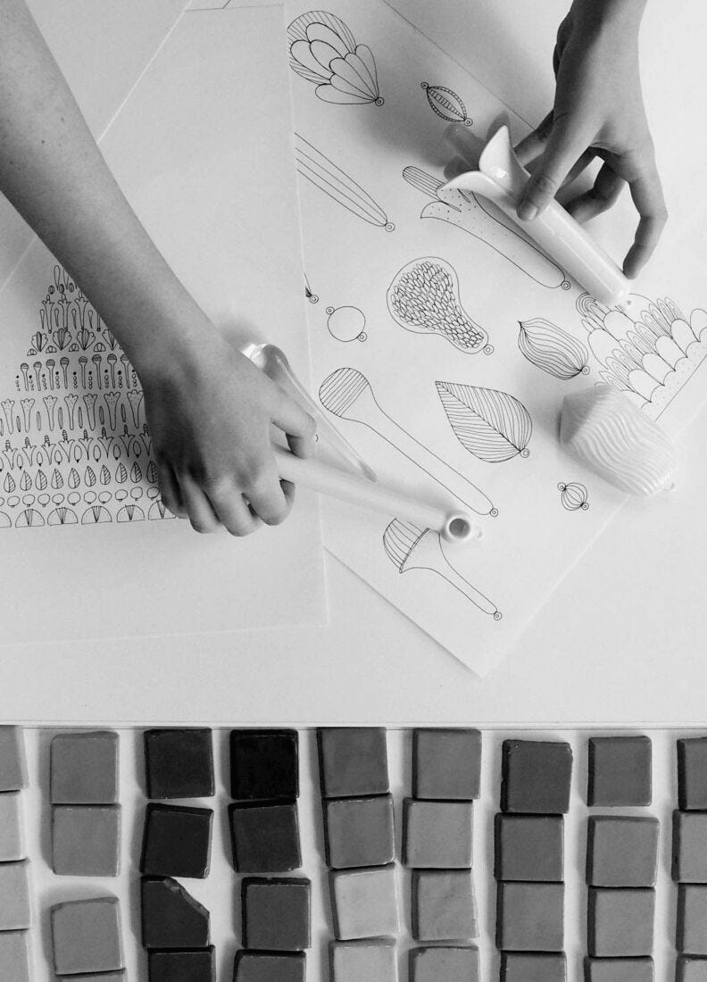 Hands working with sketches and colored porcelain tiles for Lladró - Seasons Chandelier 70 - Sunrise design.