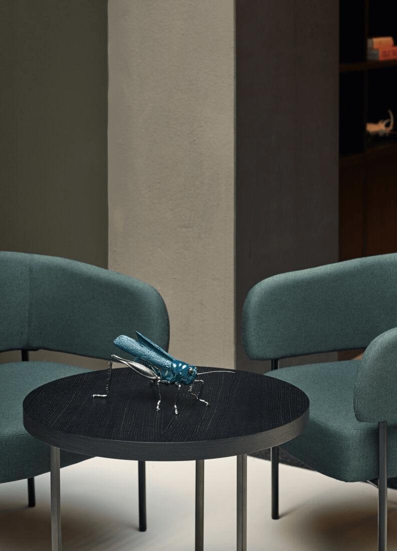 Lladró - Bee Sculpture on a black table between modern green chairs, showcasing artistry in porcelain.
