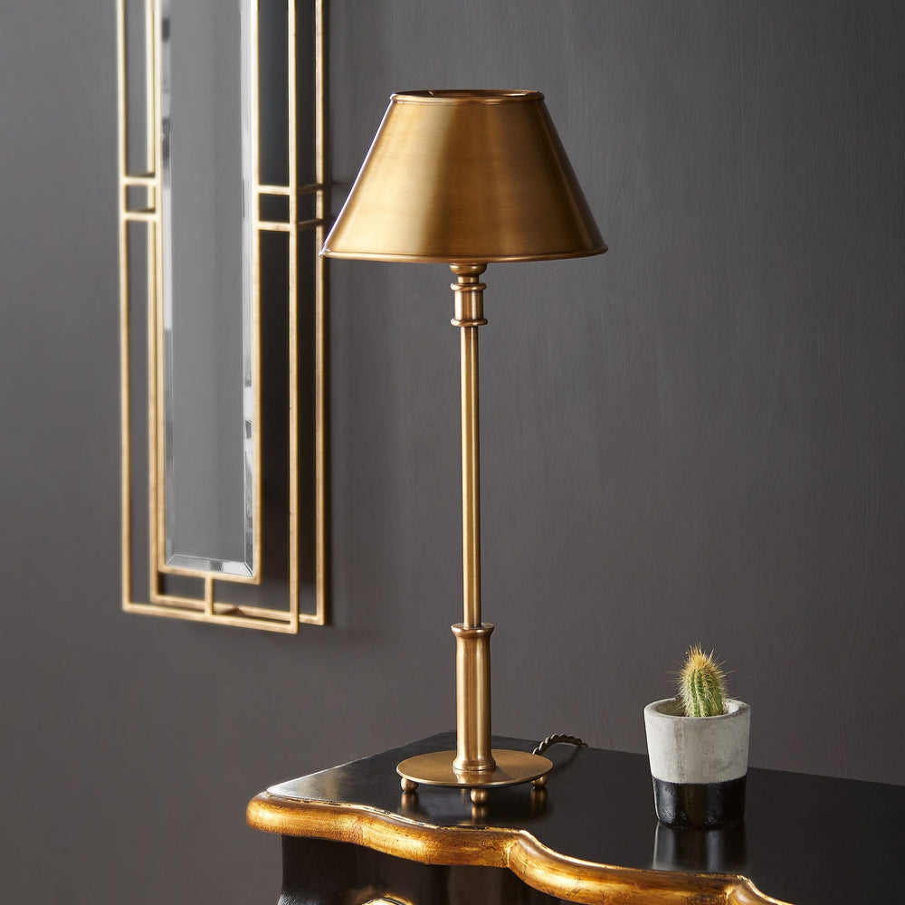Pooky - Regular Pod Table Lamp Base - Antique Brass shown with a matching brass shade, resting on ball feet on a dark table.