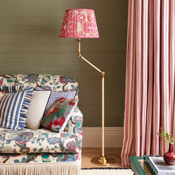 Pooky - Abel Standing Lamp Base - Brass And Natural Rattan - Without Lampshade next to a floral sofa.