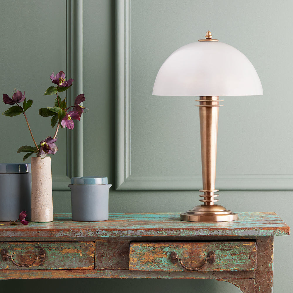 Pooky - Pietro Table Lamp - Brass and Glass on a vintage wooden console table against a green paneled wall.