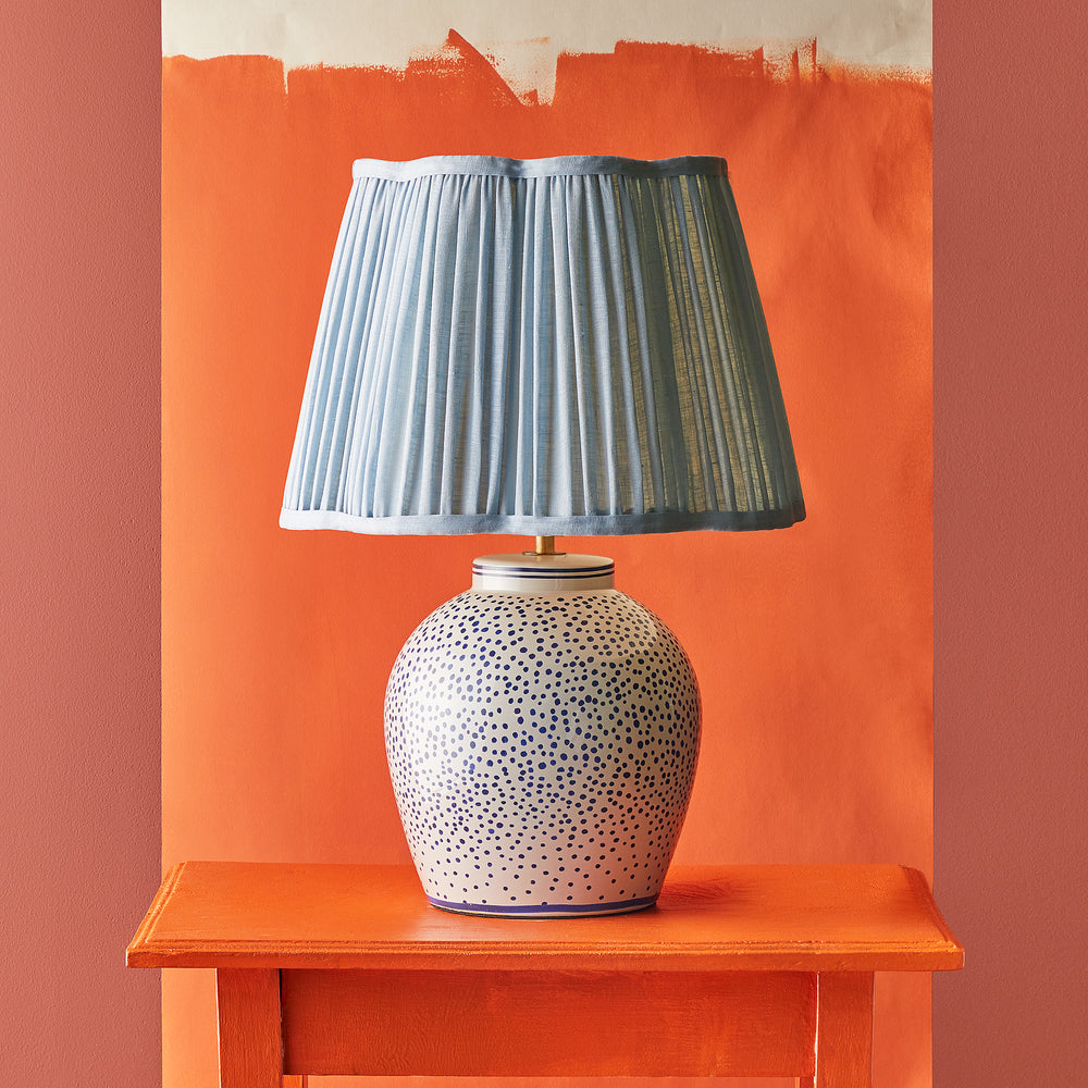 Pooky - Polka Table Lamp Base - Blue and White shown with a light blue pleated lampshade on a bright orange table.